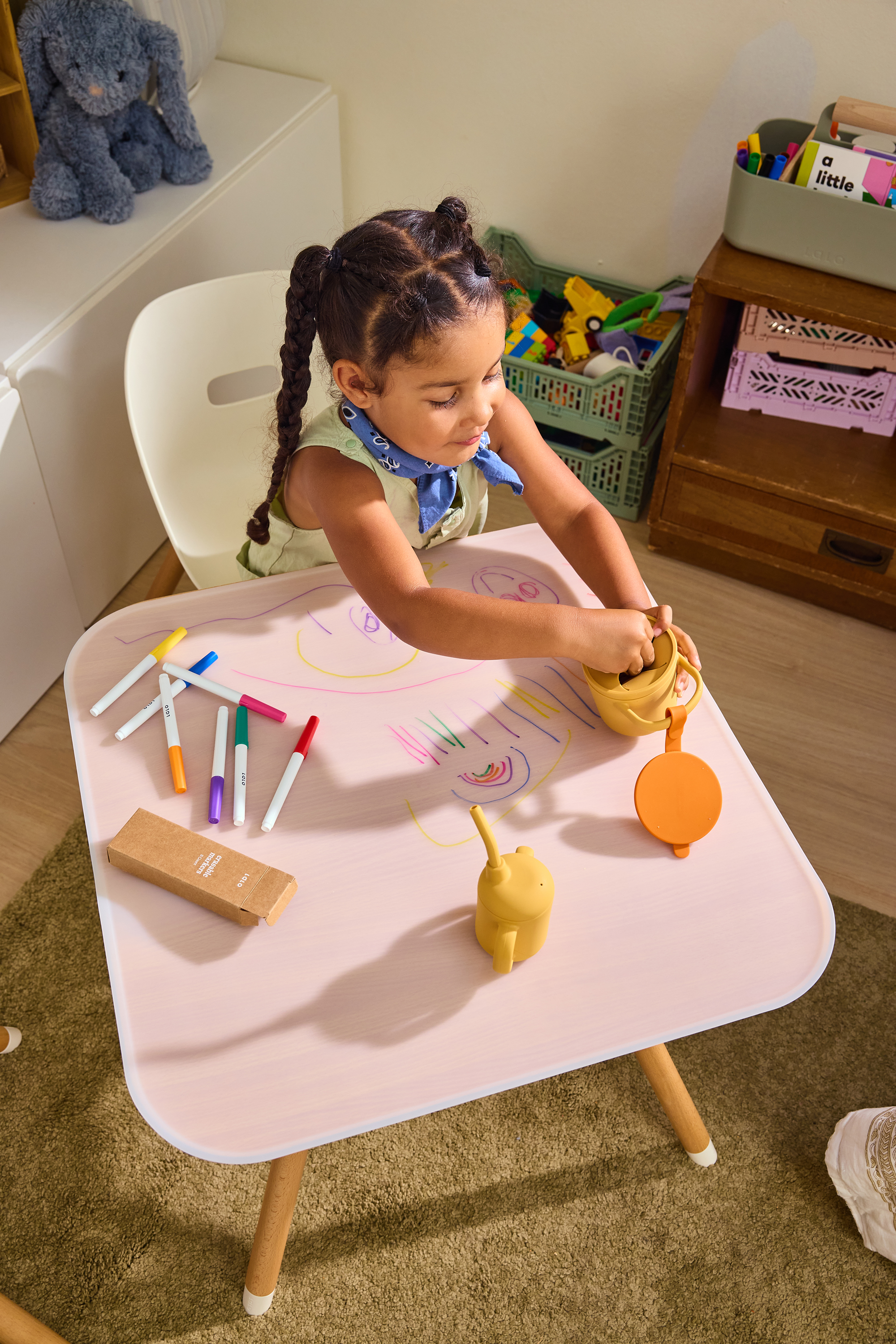 A toddler drawing at a small play table covered in colorful marker scribbles